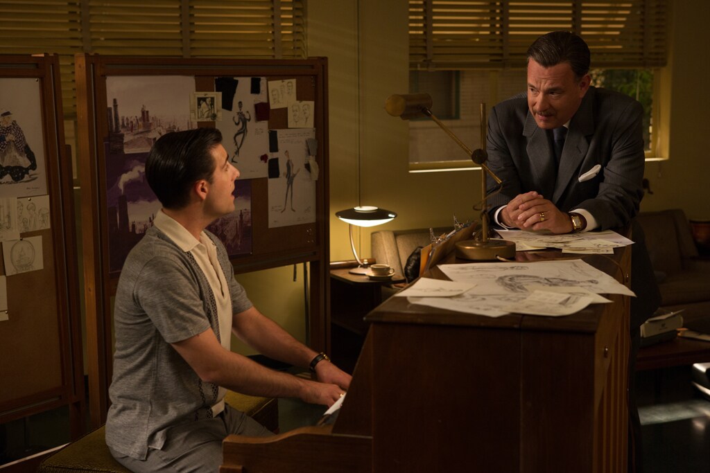 Actor Jason Schwartzman (as Richard Sherman) playing a piano and actor Tom Hanks (as Walt Disney) leaning against the piano in the movie "Saving Mr. Banks".