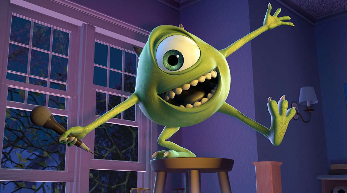 Billy Crystal as Mike Wazowski standing on a stool, holding a microphone and smiling like he just told a joke in Monsters, Inc.