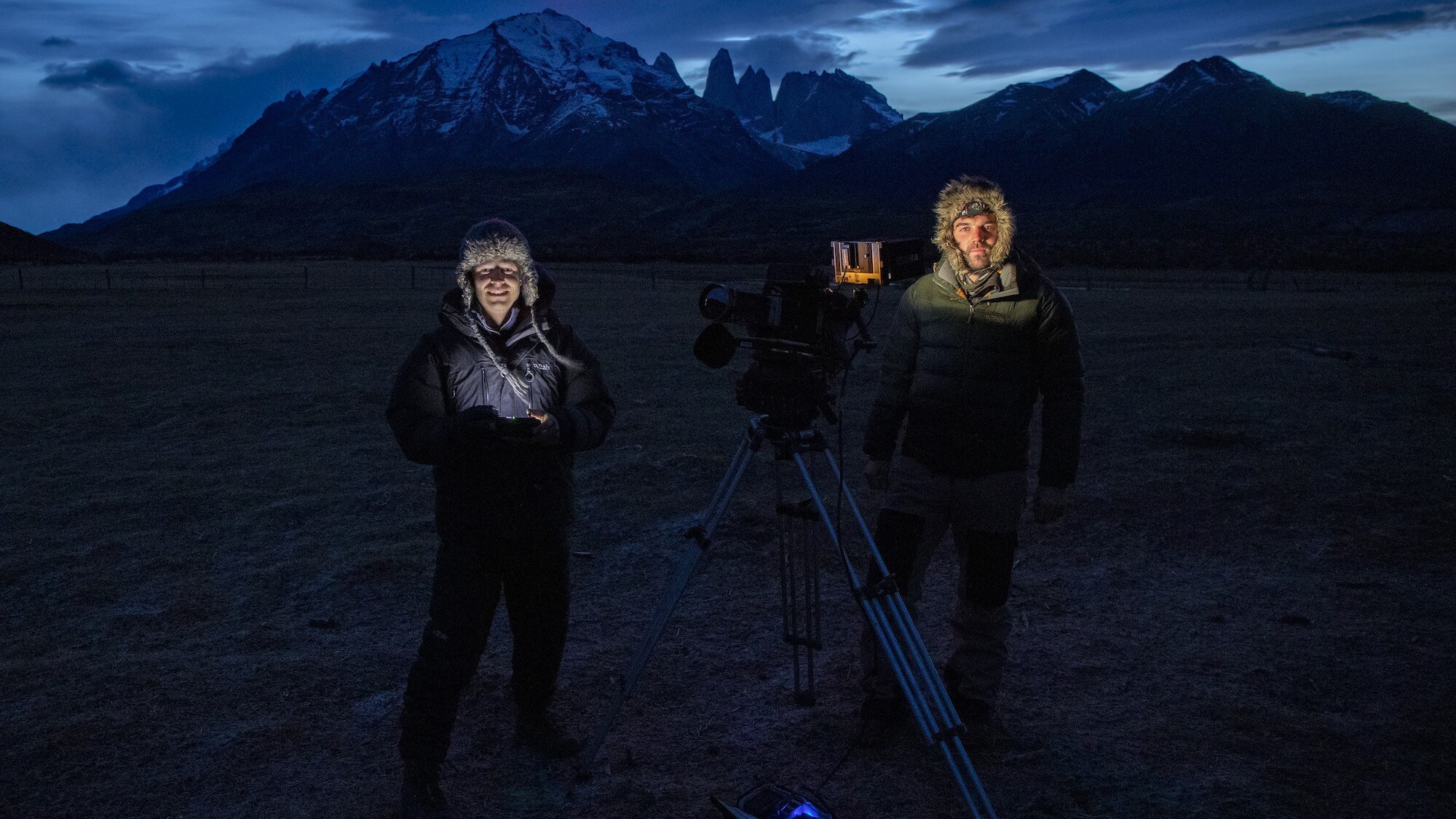 Bertie Gregory and Sam Stewart standing with camera in front of the mountains.  (National Geographic for Disney+/Bertie Gregory)
