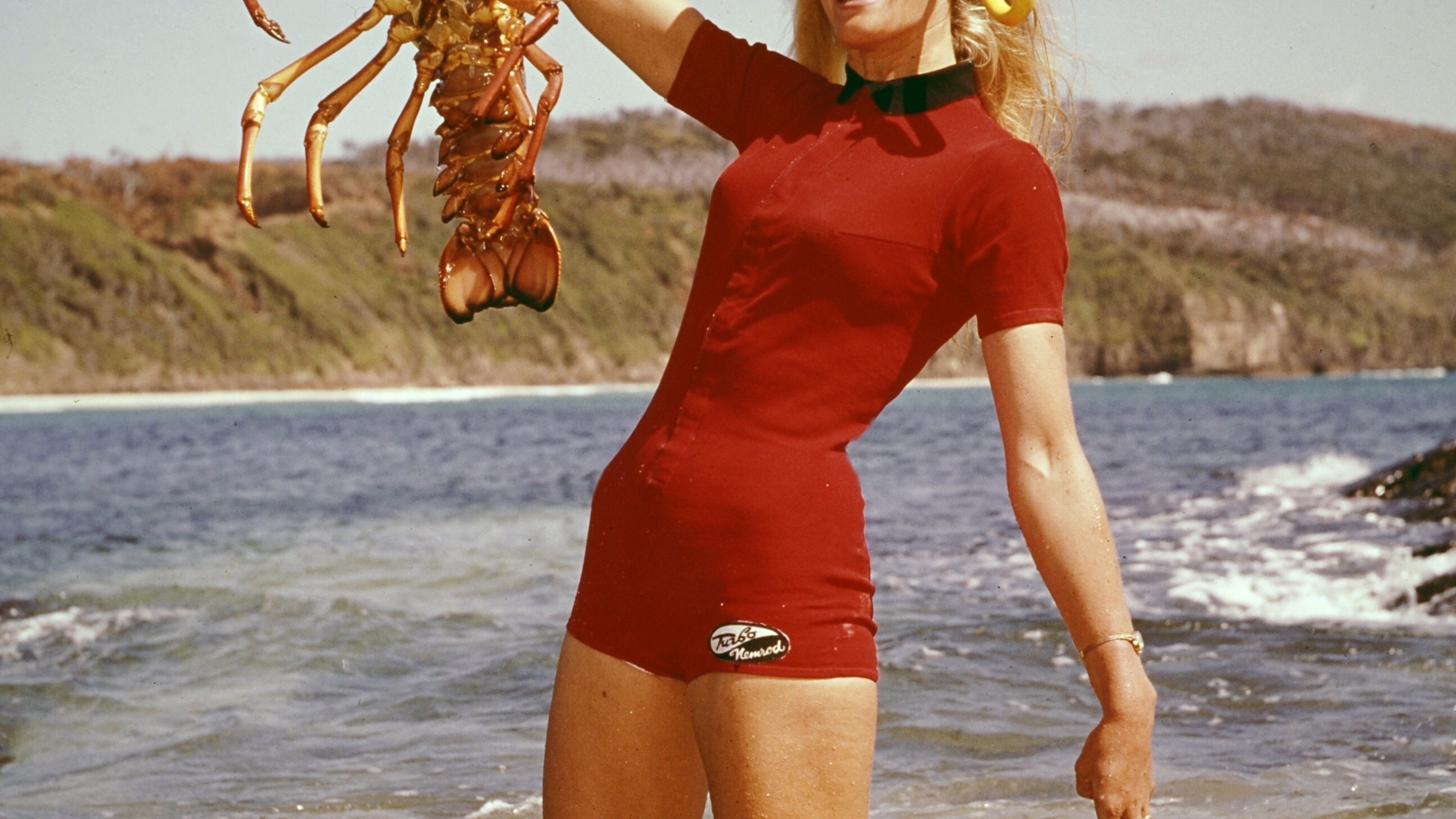 Valerie Taylor in red swimsuit holding up a crayfish in 1960.  (photo credit: Ron & Valerie Taylor)