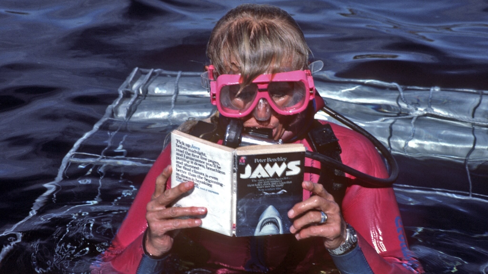 Valerie Taylor in scuba gear reading the Jaws book on top a shark cage in 1982.  (photo credit: Ron & Valerie Taylor)