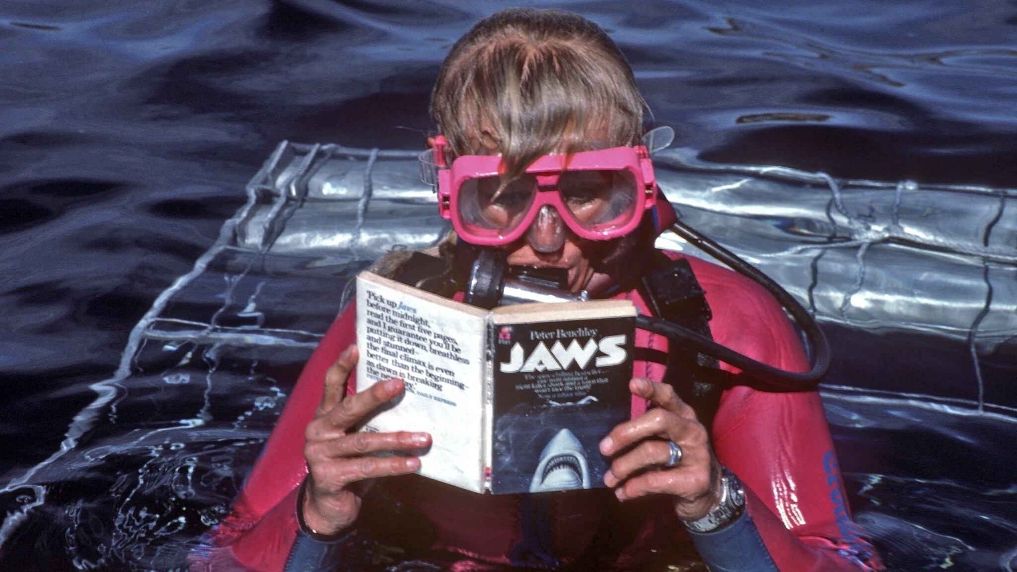 Valerie Taylor in scuba gear reading the Jaws book on top a shark cage in 1982. (photo credit: Ron & Valerie Taylor)