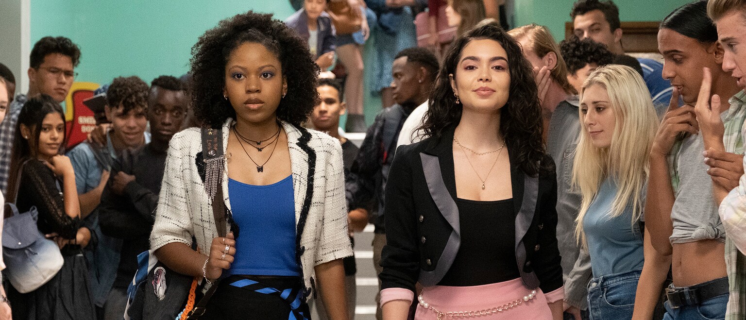 Image of Darby Harper (actor Riele Downs) and Capri (actor Auli'i Cravalho) walking down a classroom hallway, from the 20th Century Studios movie, "Darby and the Dead".