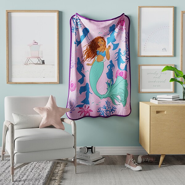 Image of a Little Mermaid throw blanket hanging on a wall in a furnished room.