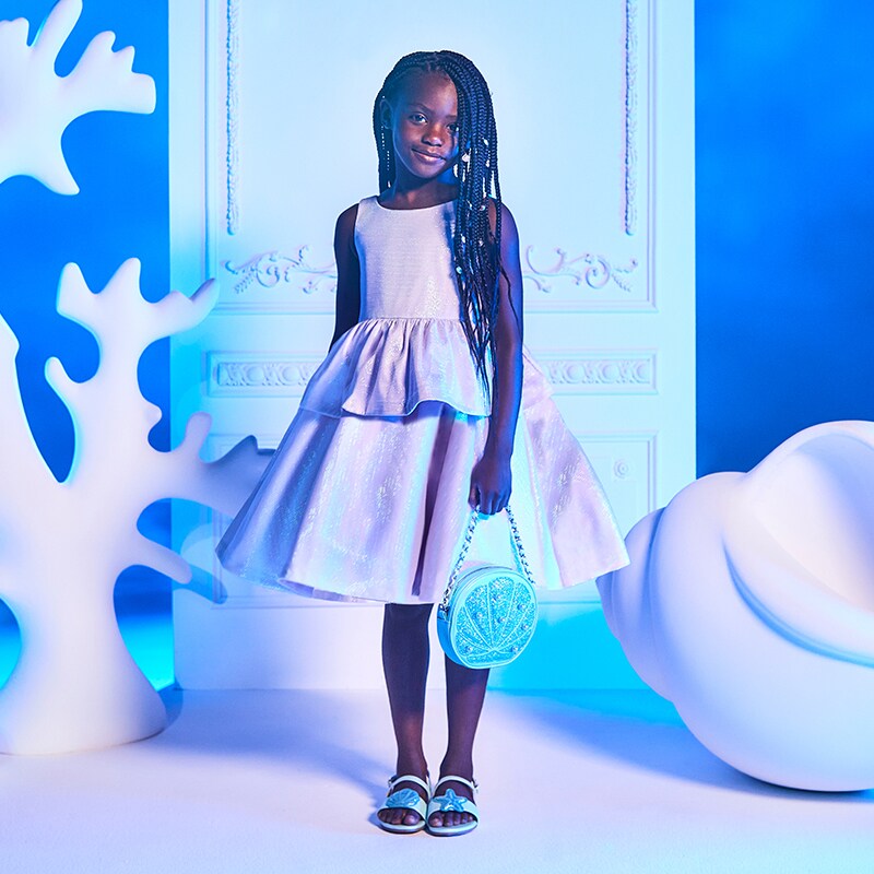 Image of a girl wearing a dress, sandals, and a shell-design purse from the Janie & Jack collection.