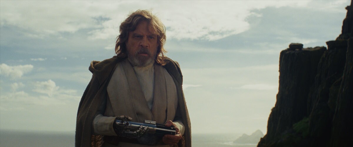 An aged Luke Skywalker holding his father's lightsaber on Ahch-To