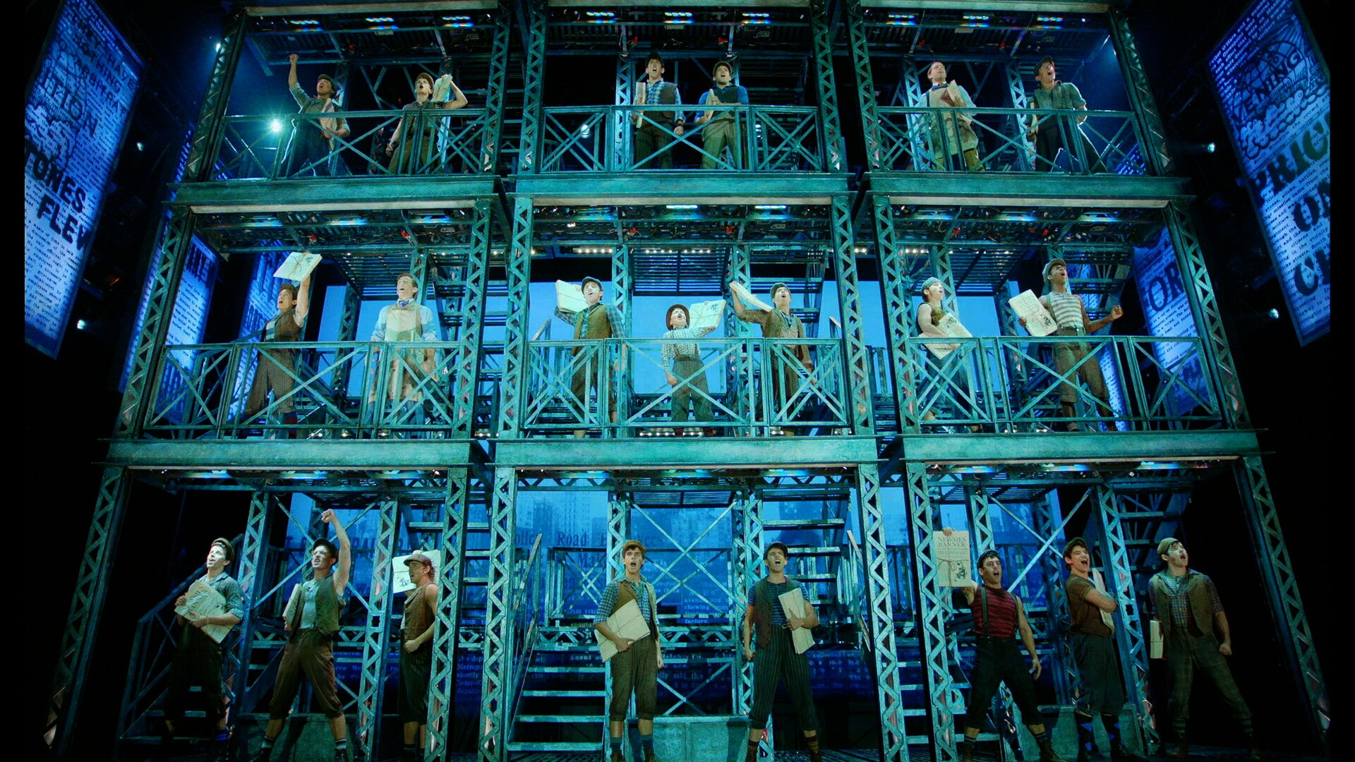 The Newsies cast performing on stage on a tiered structure