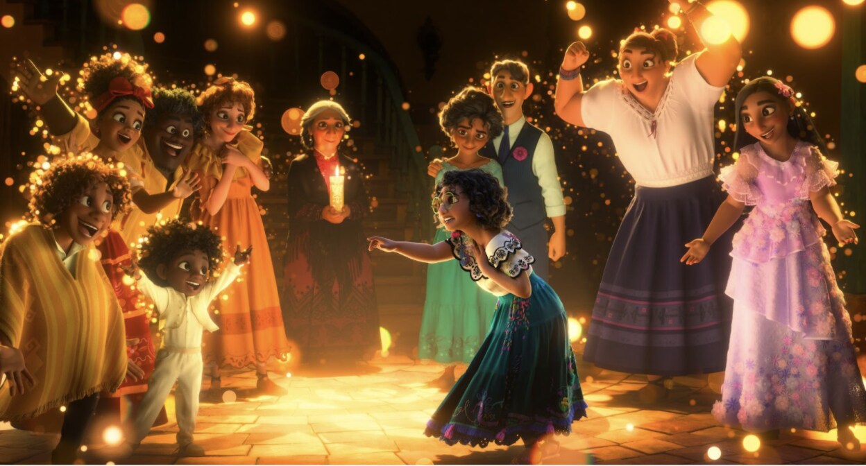 Mirabel points and smiles as the Madrigal family surrounds her in celebration in Walt Disney Animation Studios' Encanto