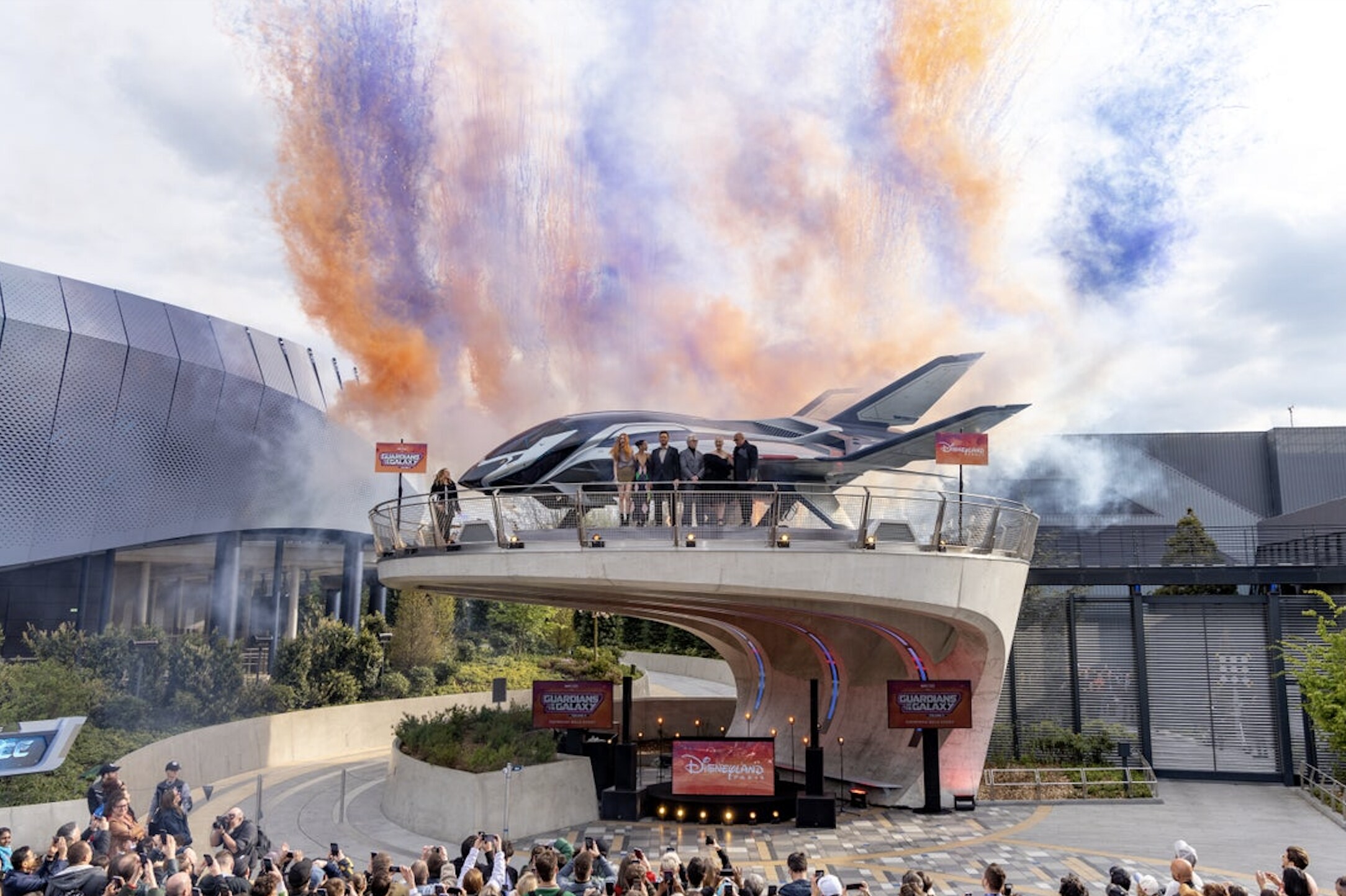 Guardians of the Galaxy Vol. 3 cast and director stood in front of the Quinn jet at Disneyland Paris with orange and purple smoke behind them.