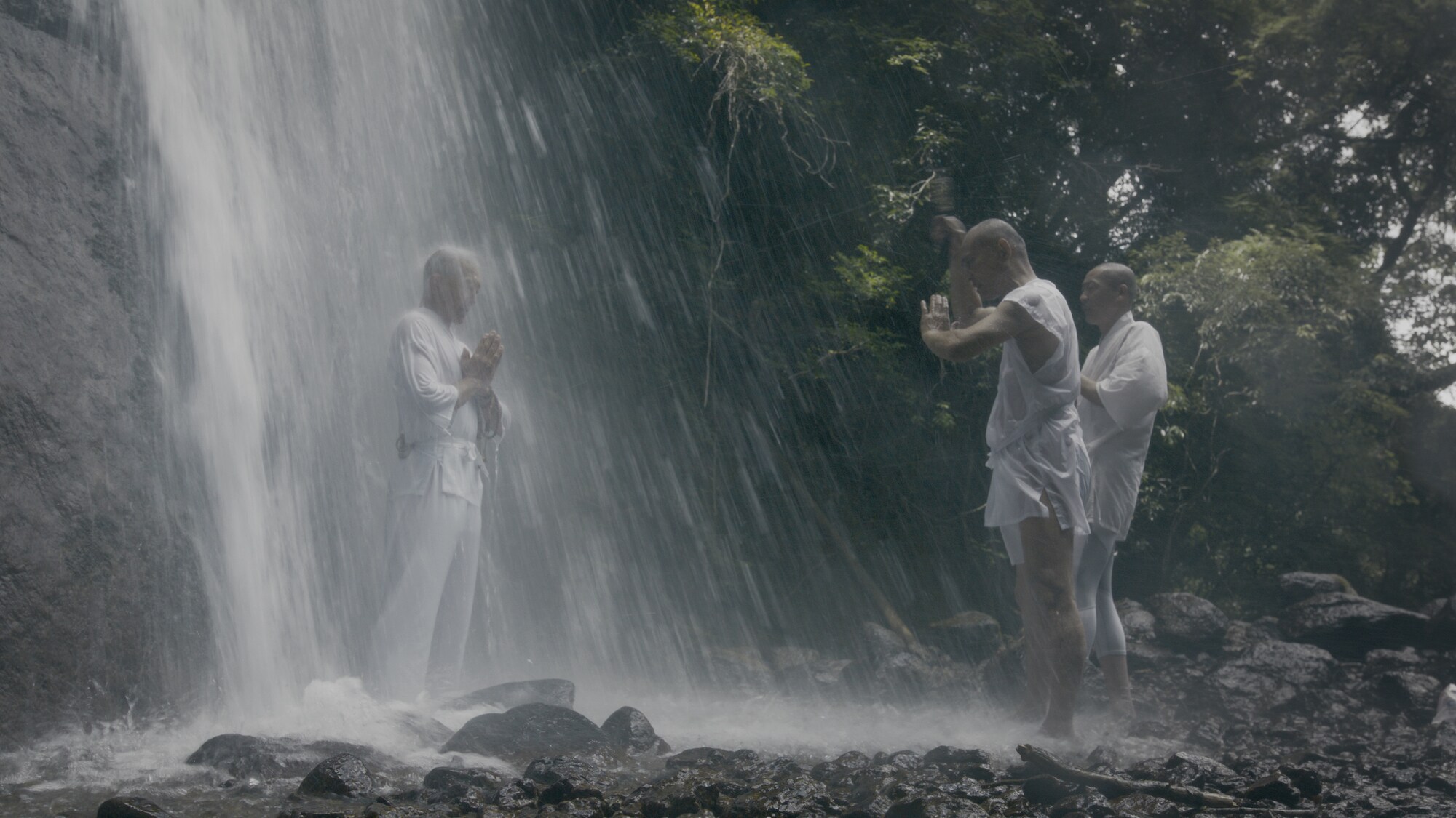 Monks stand under a waterfall. (National Geographic for Disney+)