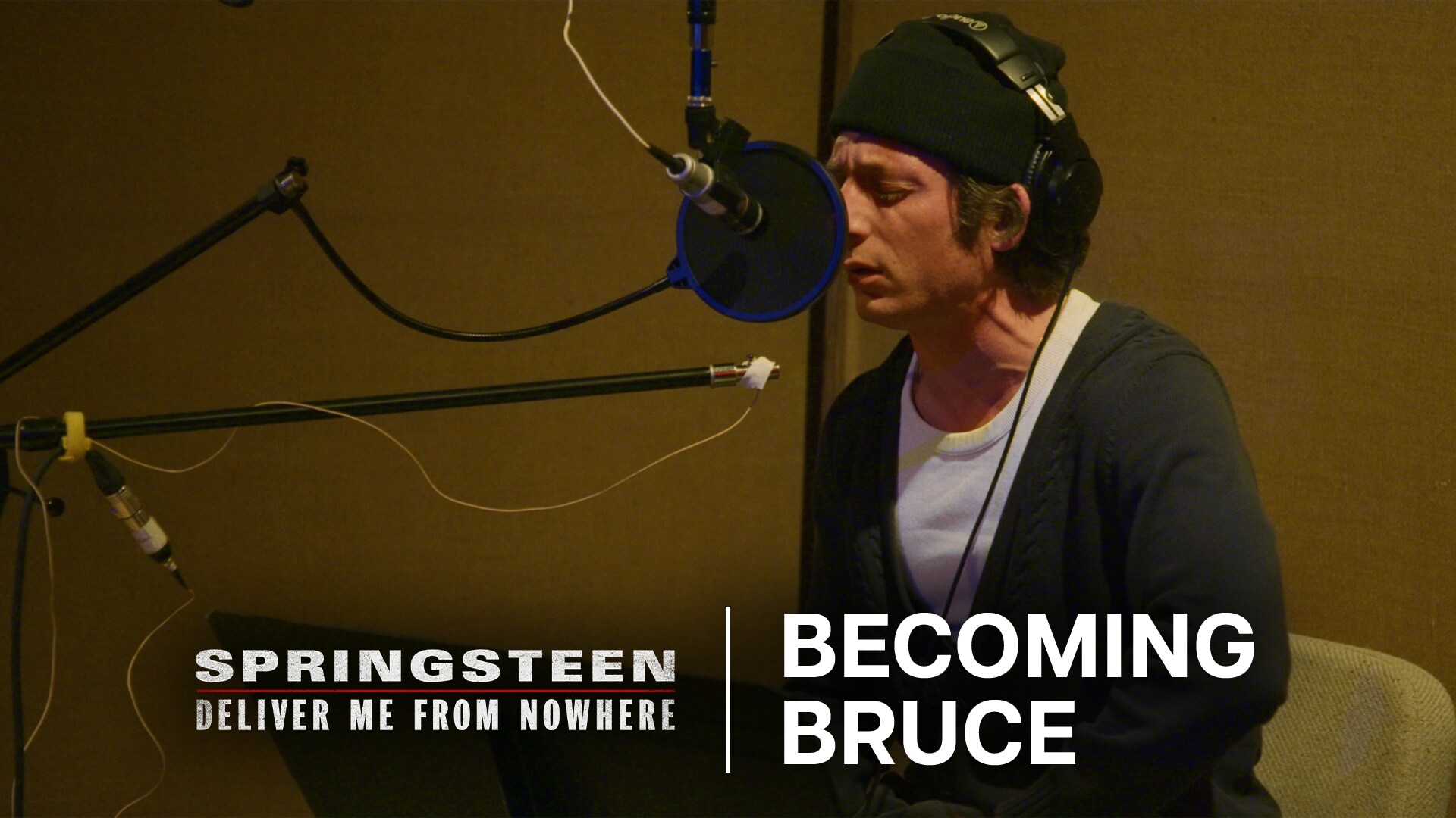 Image of actor Jeremy Allen White wearing headphones and singing into a microphone in a recording studio. | Springsteen: Deliver Me From Nowhere | Becoming Bruce