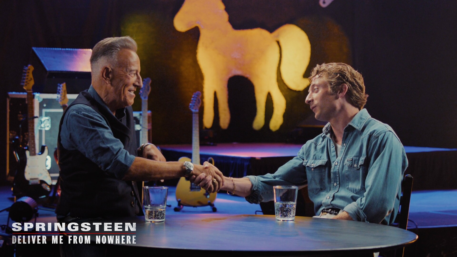 Image of Bruce Springsteen and actor Jeremy Allen White shaking hands while sitting at a table. | 20th Century Studios | Springsteen: Deliver Me From Nowhere