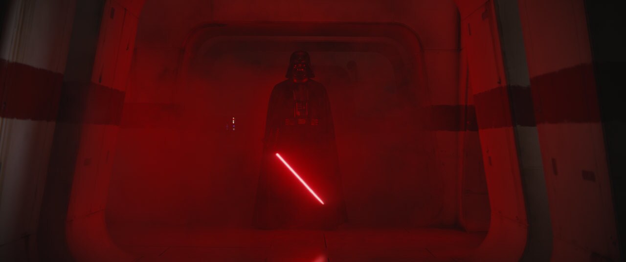 Darth Vader arrives, chasing the Death Star plans down a darkened corridor with the glow of his red saber to light the way in Rogue One: A Star Wars Story.