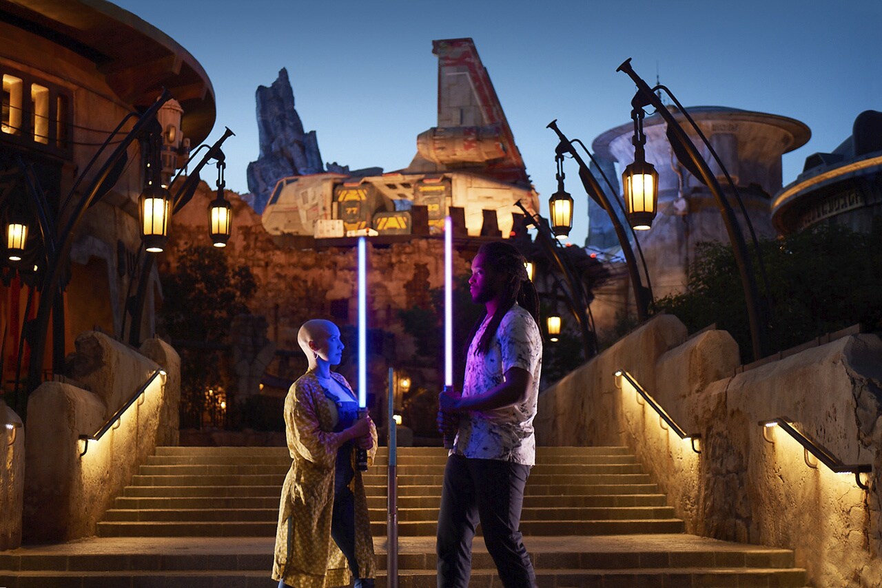Two people stand with their lightsabers lit at Disneyland