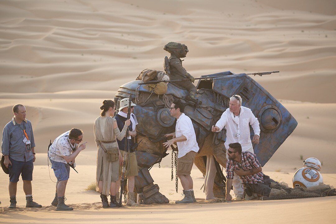 Daisy Ridley and J.J. Abrams, third and fifth from left, talk to some of the crew behind the luggabeast puppet on set of Star Wars: The Force Awakens.