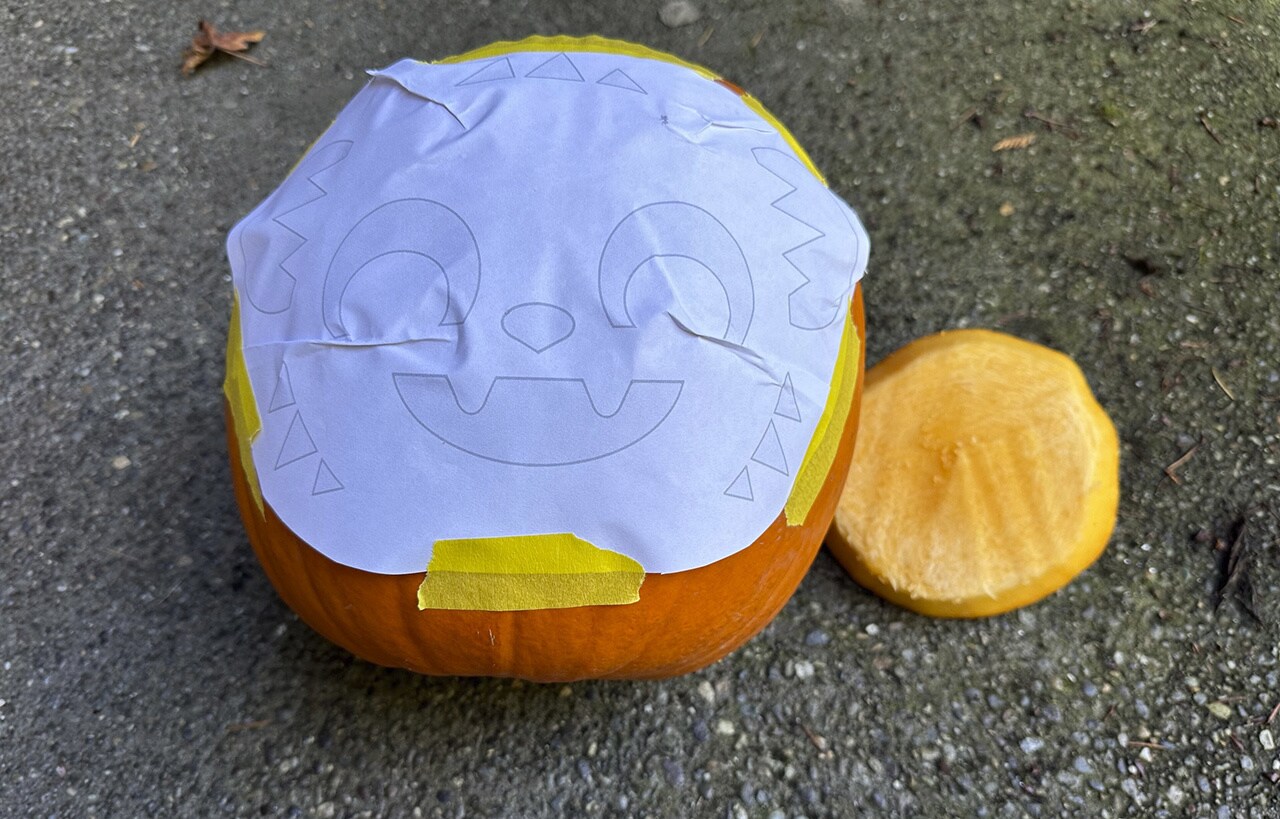 Step 3: Choose the side of the pumpkin you’d like to use for Nubs. Use the masking tape to attach the stencil to that side, slightly creasing the paper so that it’s pressed against the pumpkin as close as possible.