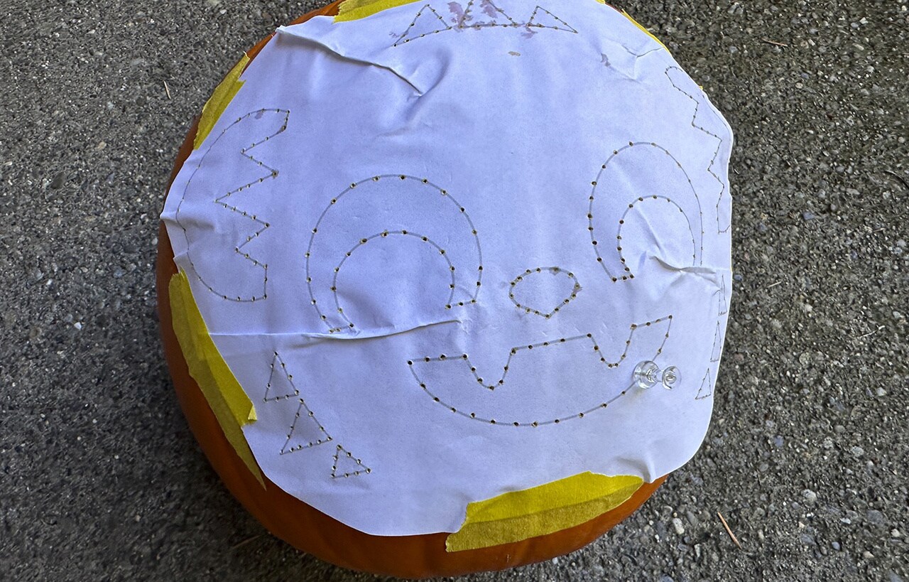 Step 4: Trace every line of the stencil by pressing the pushpin through the paper and into the pumpkin. The more holes you poke, the easier it will be to connect the dots when carving!