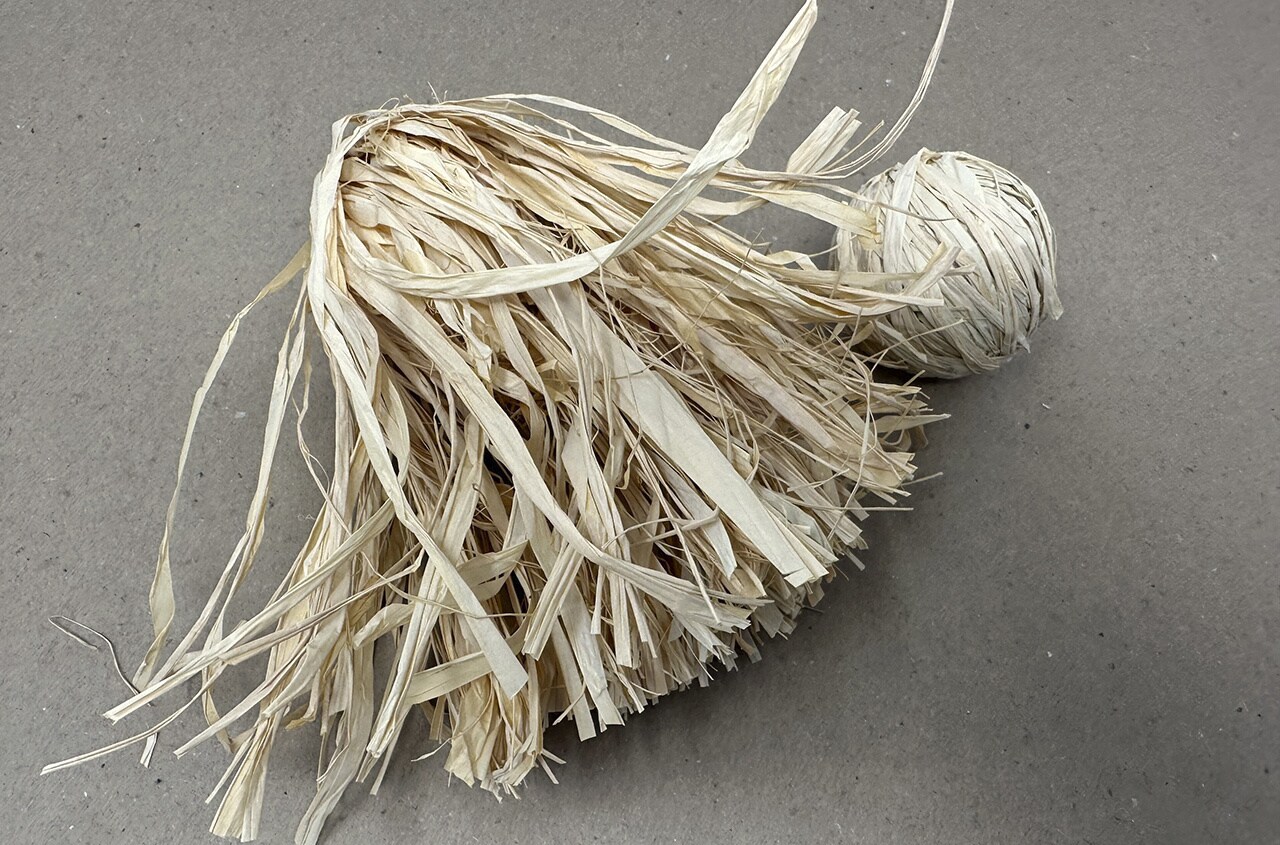 Step 10: Glue down the raffia to the sides of the ball as needed to completely cover the body in vertical pieces of straw.