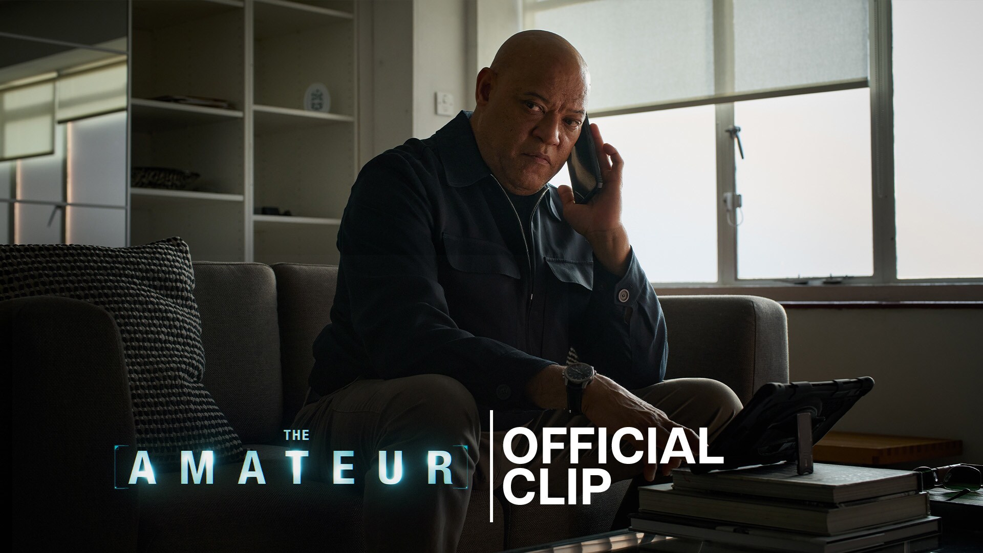 Image of actor Laurence Fishburne sitting on a couch with a mobile phone to his ear. From the 20th Century Studios movie, "The Amateur."