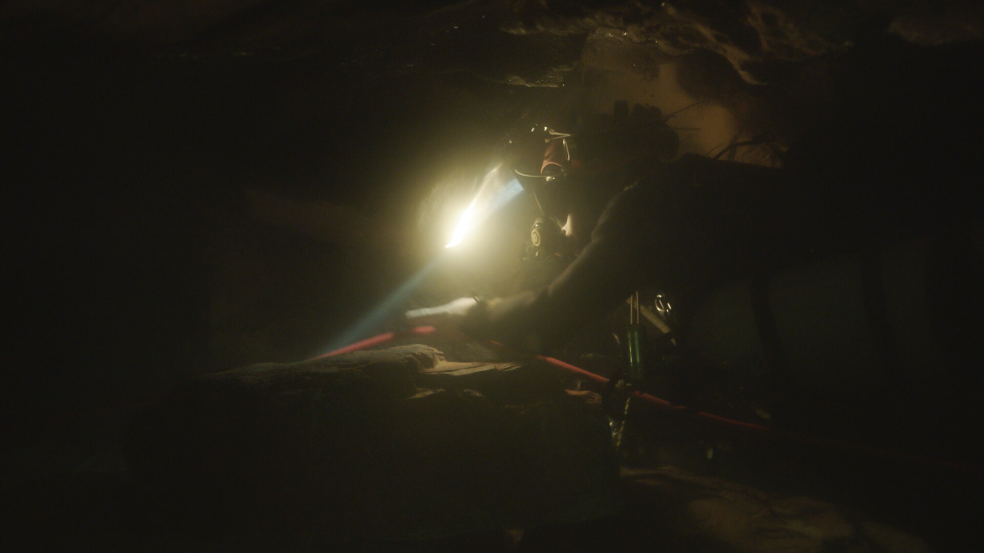 A diver swims through a dark cave guided by a headlamp.  THE RESCUE chronicles the 2018 rescue of 12 Thai boys and their soccer coach, trapped deep inside a flooded cave. E. Chai Vasarhelyi and Jimmy Chin reveal the perilous world of cave diving, bravery of the rescuers, and dedication of a community that made great sacrifices to save these young boys. (Credit: National Geographic)