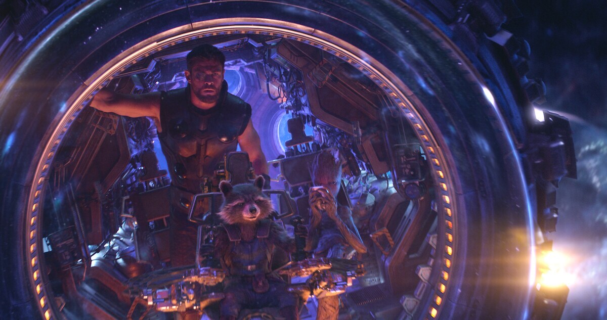 Thor, Rocket, and Groot sit in a space ship, in purple lighting in a scene from Avengers: Infinity War. 