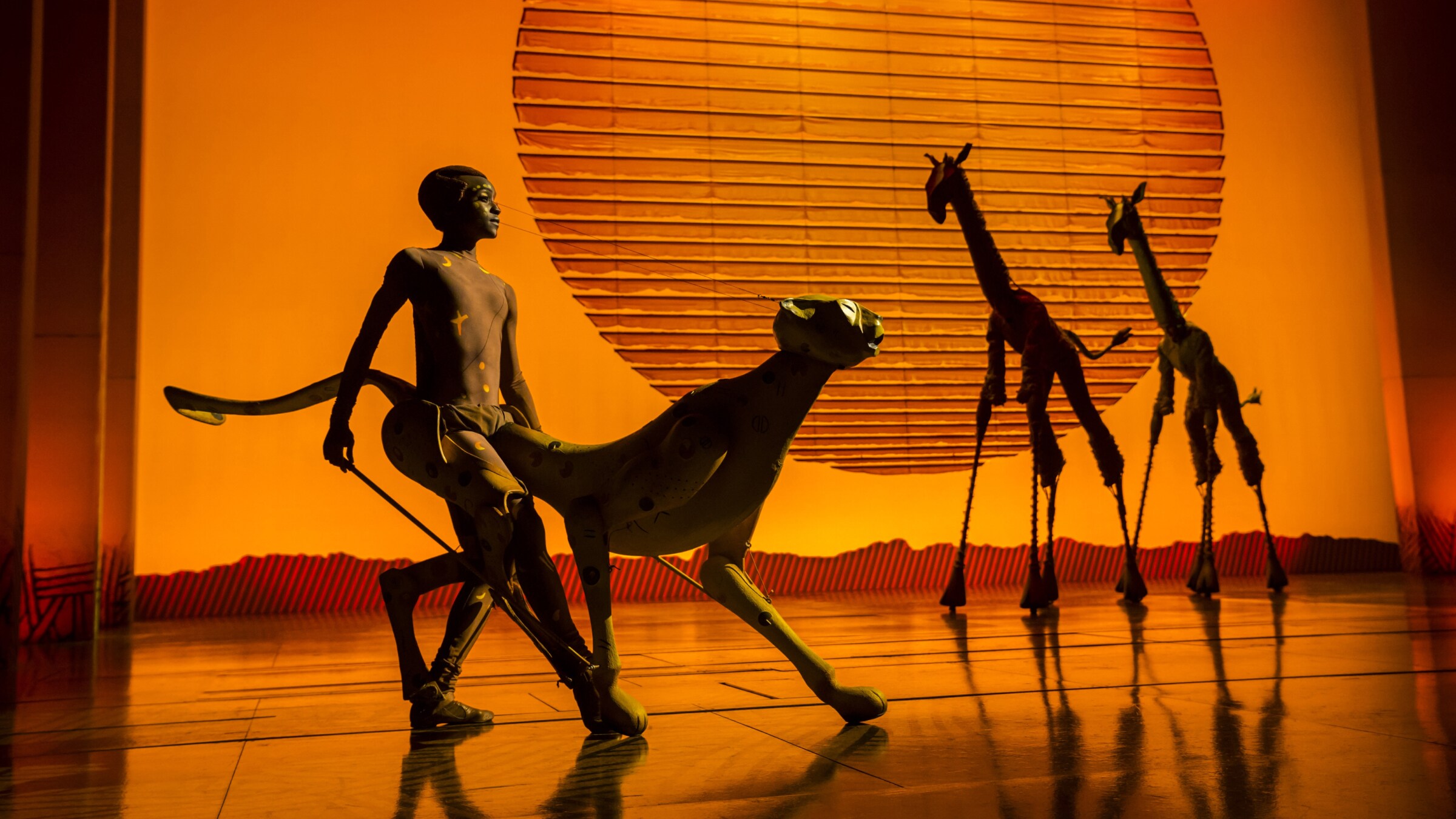 Cast members on stage in different animal costumes, including giraffes. 