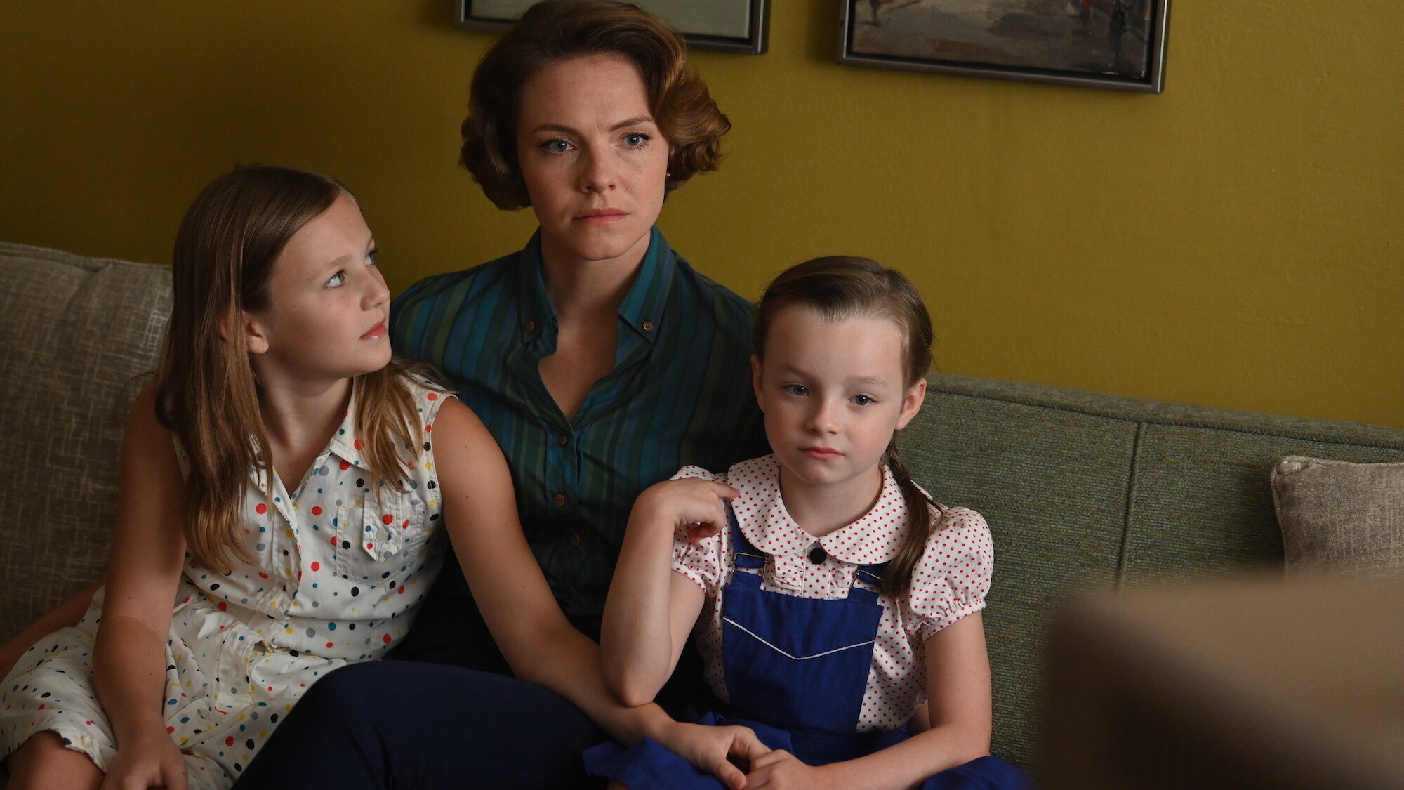 Trudy Cooper, played by Eloise Mumford, watches a press conference on TV with her daughters in National Geographic's THE RIGHT STUFF streaming on Disney+. (Credit: National Geographic/Gene Page)