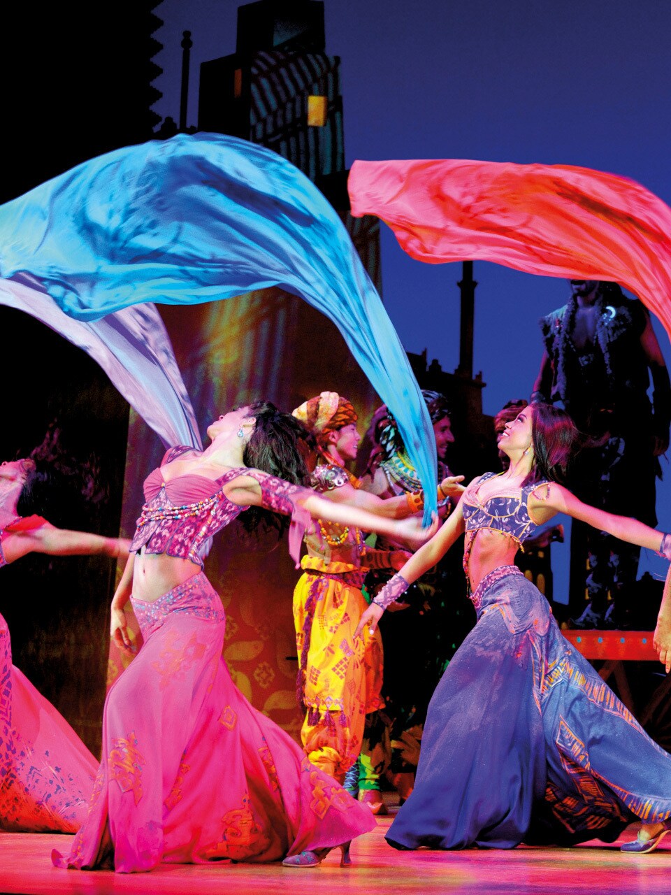 The Aladdin ensemble on stage dancing with colourful silks. cloths floating.