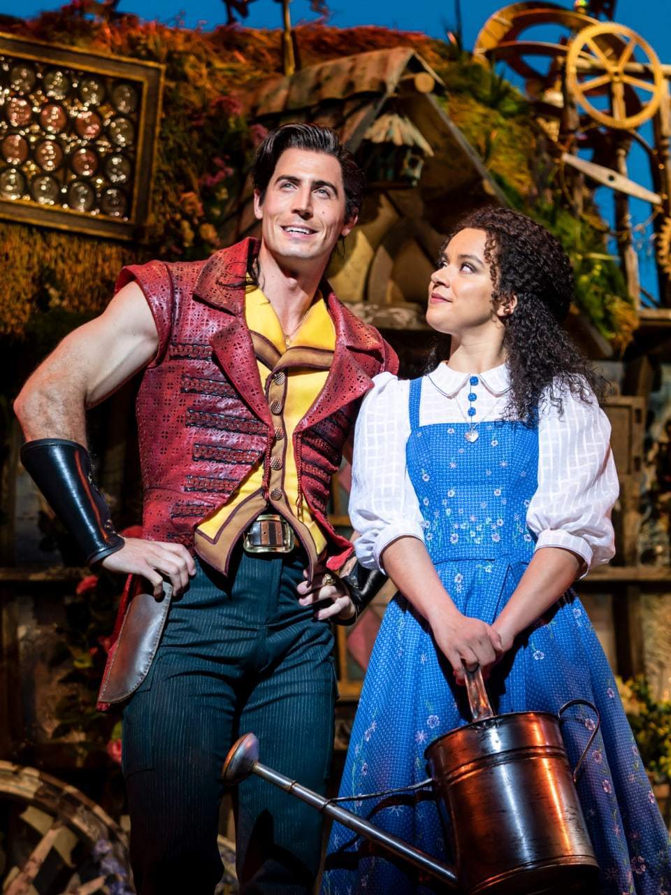 Tom Senior as Gaston and Courtney Stapleton as Belle in front of a little house on a village background.