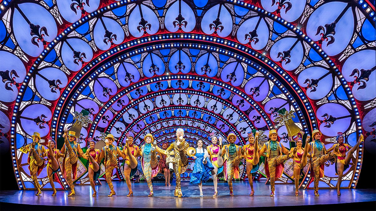 Lumiere and Belle lead the dance with the ensemble dressed in colourful costumes.