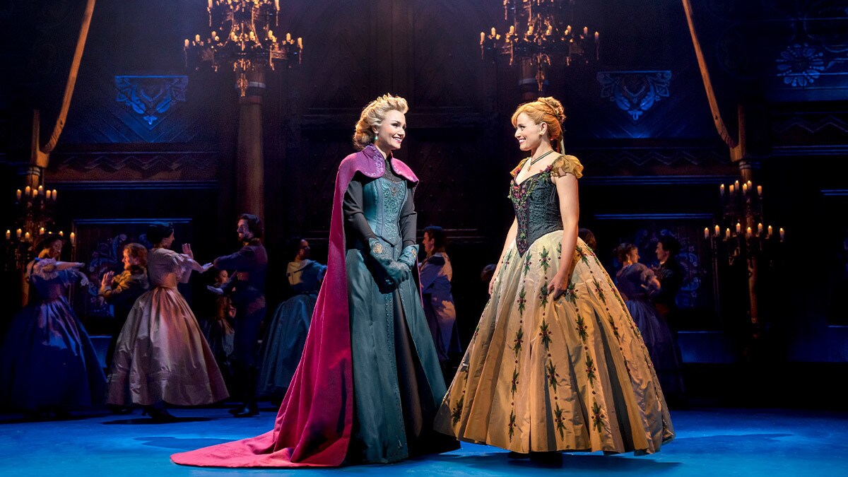 Elsa and Anna smiling at each other at a ball in the kingdom palace.