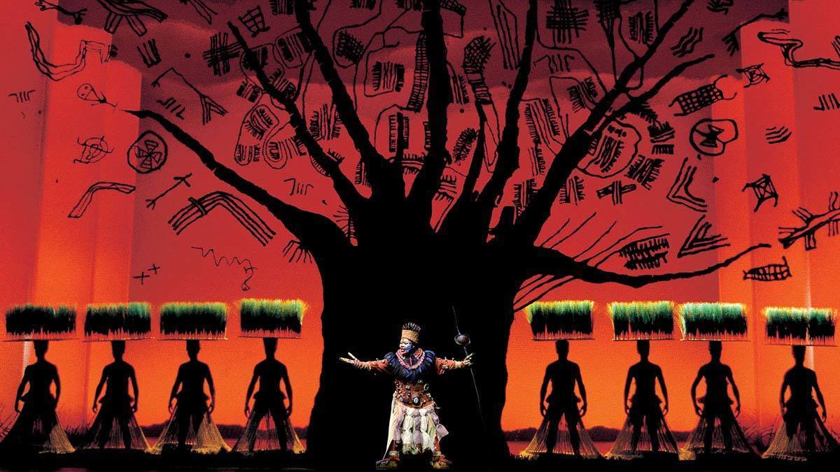 Rafiki in front of a silhouette of a tree in the stage show The Lion King