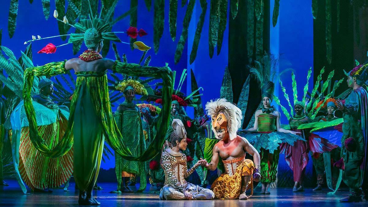 Simba and Nala surrounded by actors posing as greenery in the stage show The Lion King