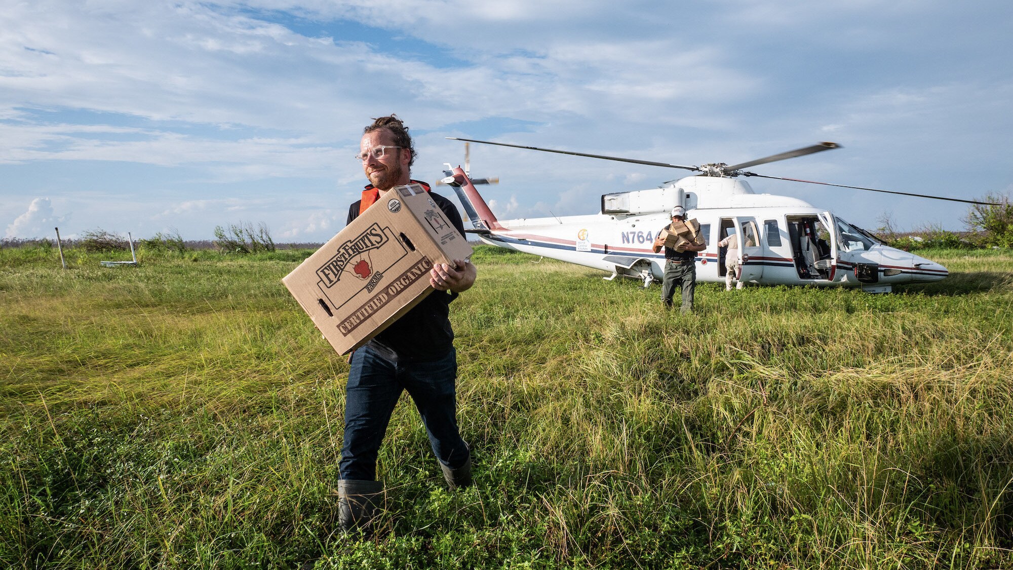 Sam Bloch, WCK's Director of Emergency Response, carries a box in field from helicopter. (Credit: National Geographic/Sebastian Lindstrom)