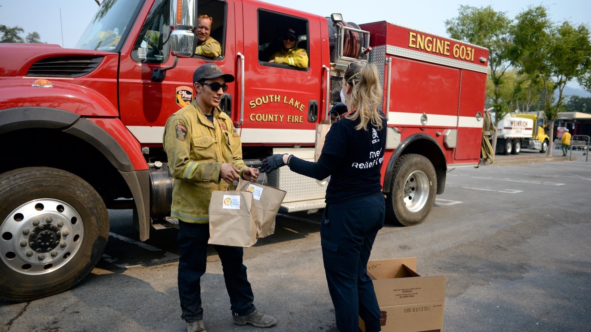 World Central Kitchen Operations Lead, Anna Bornstein (R), hands WCK food bags to CalFire firefighters headed back to fight a wildfire. (Credit: National Geographic/Kelly Galleguillos)