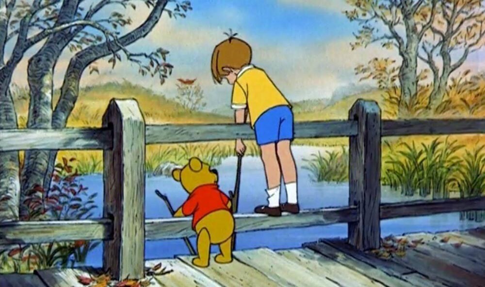 Animated Characters Winnie the Pooh (teddy bear) and Christopher Robin holding sticks over a bridge