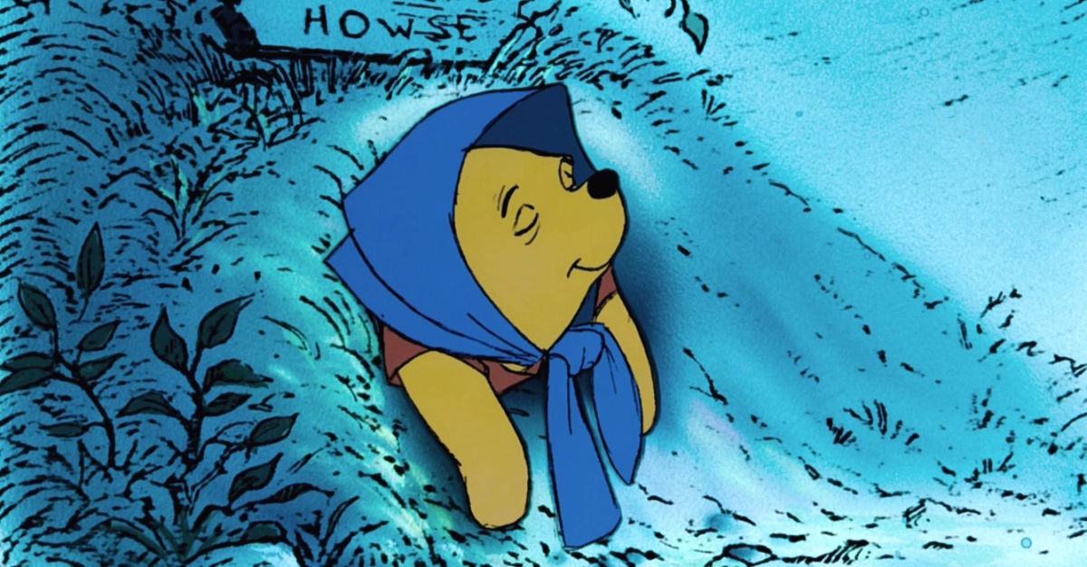 A sleeping Winnie the Pooh hanging out of his hole while wearing a blue bonnet